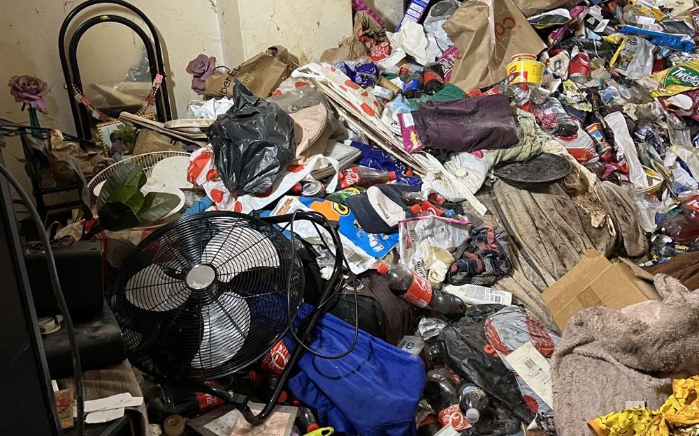 A severely hoarded room on a real Hoarder Cleanup job, belongings piled to waist height